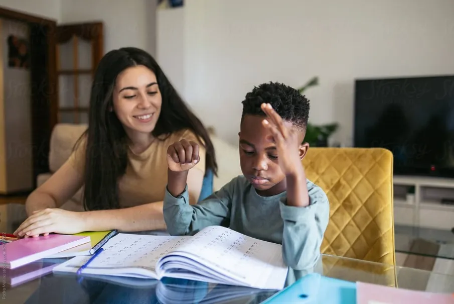 Young boy studying with a woman assisting him at home.