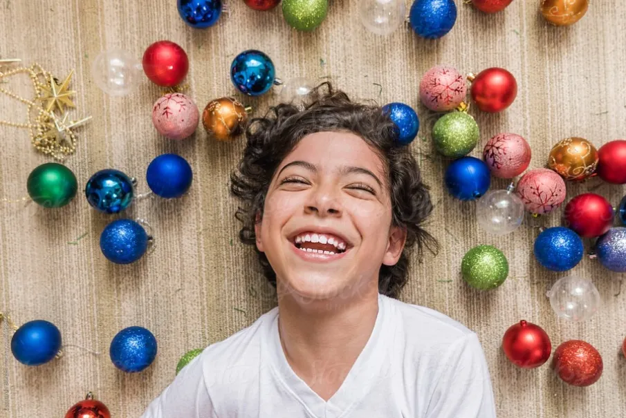 Joyful child surrounded by colorful Christmas ornaments.