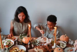 Family enjoying a Thanksgiving meal with decorative pumpkins and candles on the table.