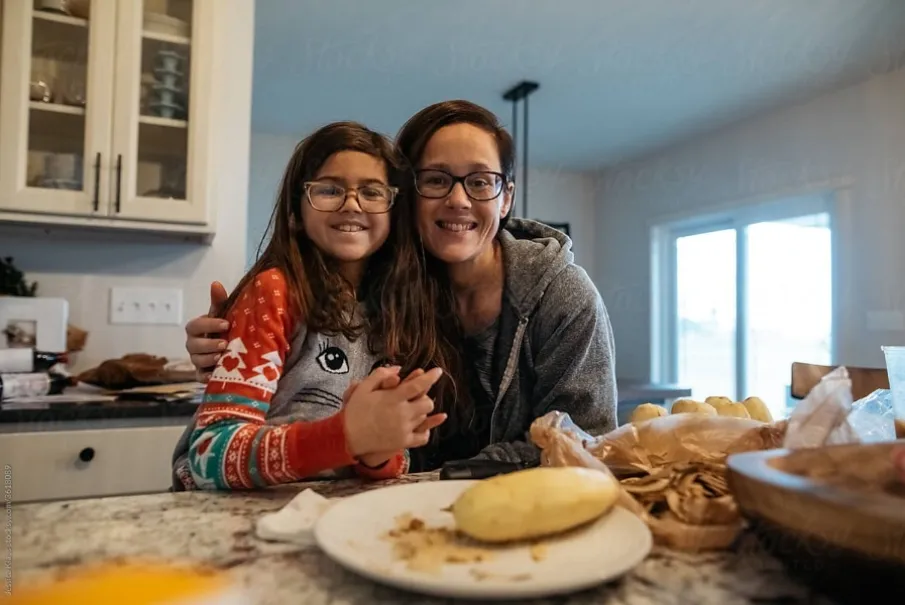 Mother and daughter smiling in a cozy kitchen while preparing food