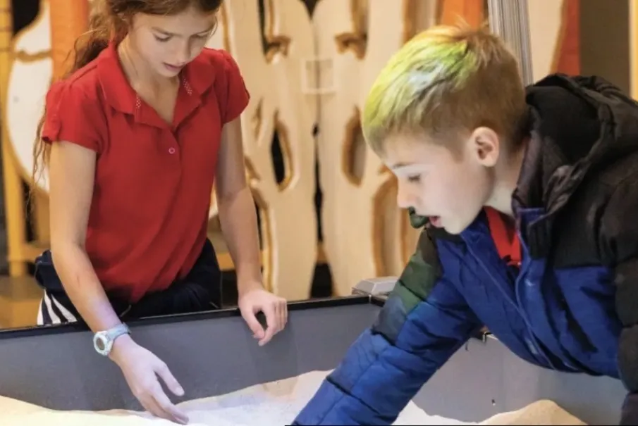 Children playing with interactive sand display at a museum
