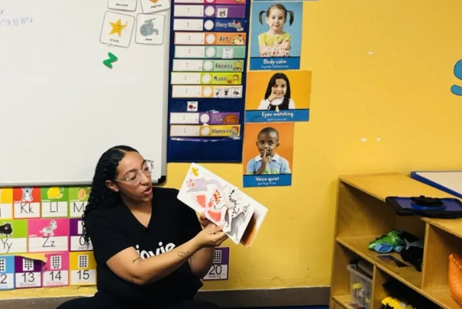 Teacher reading a book to children in a colorful classroom setting.