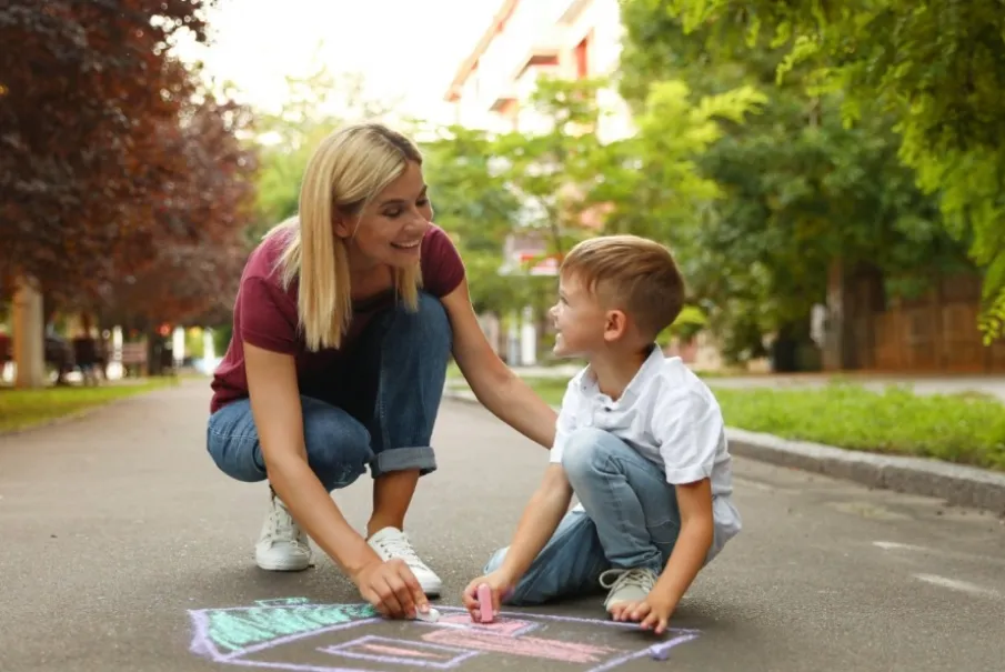 Woman drawing with boy on sidewalk with chalk