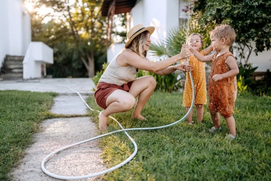 Mother playing with children using garden hose
