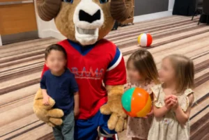 Children posing with a ram mascot holding colorful balls in an indoor play area.