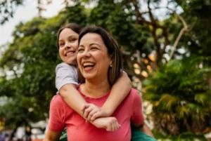 A joyful woman giving a piggyback ride to a child in a park.