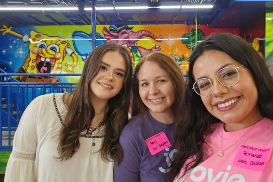 Group of smiling women posing in front of colorful mural at a fun event