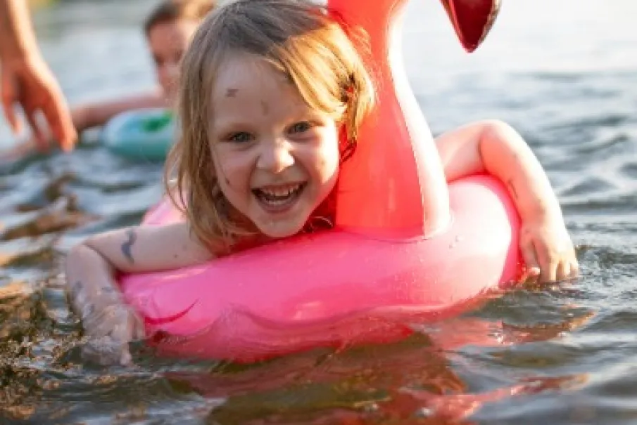 Smiling child floating on a pink flamingo inflatable in a sunny lake.