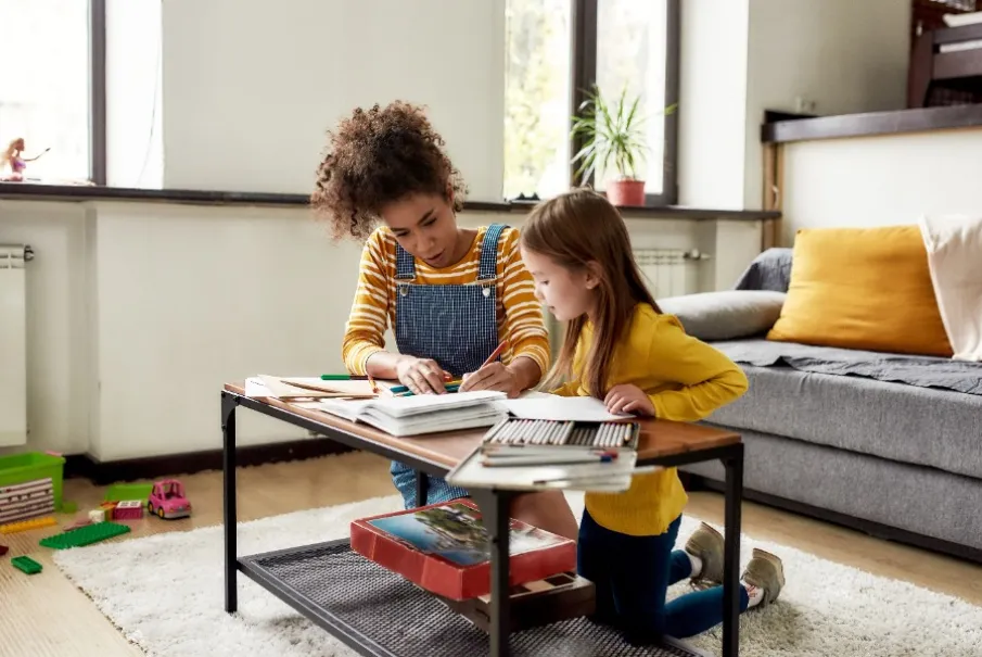 Parent helping child with homework at a living room table.