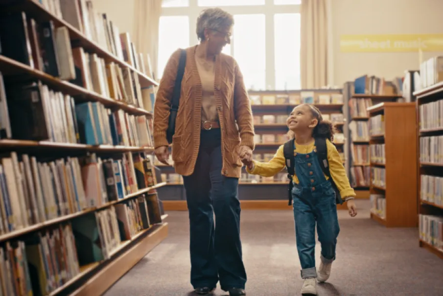Senior woman and young girl walking hand in hand in a library aisle