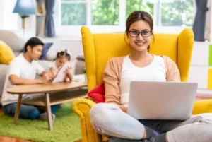 Mother working on a laptop while father helps child with homework in the background.