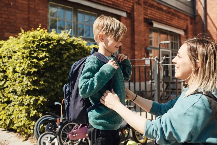 Mother helping young boy with backpack outside school