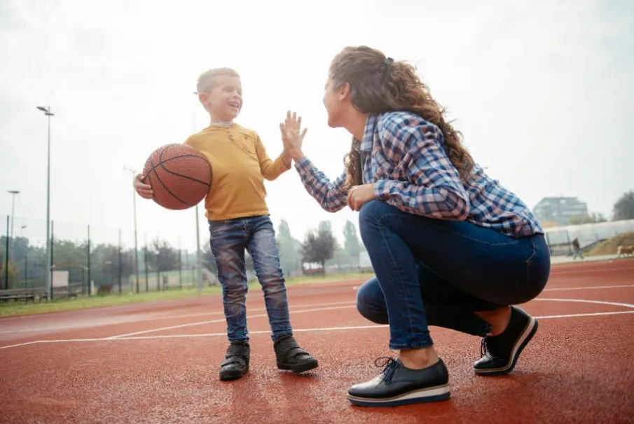 Child high-fiving woman with basketball on outdoor court