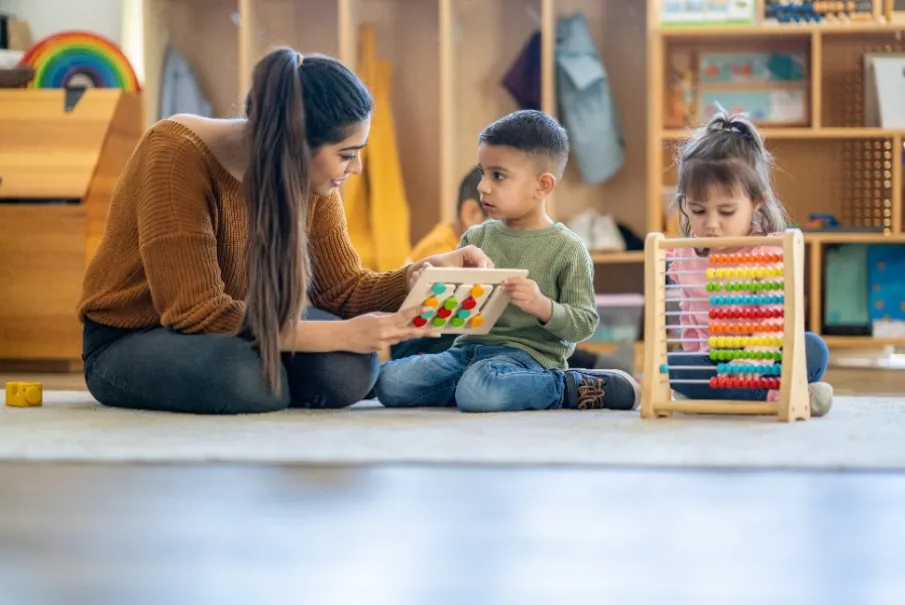 Teacher interacting with children in a classroom using educational tools and an abacus.