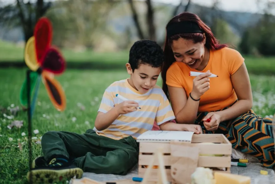 Mother and child enjoying a creative activity in the park with a colorful windmill in the background