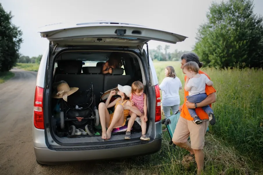 Family preparing for a picnic outing with open van trunk in countryside setting
