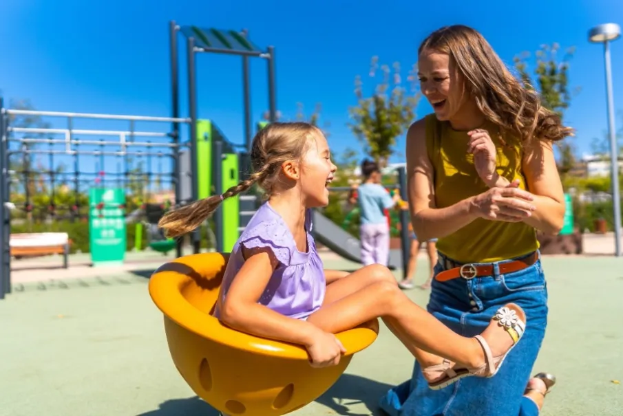 Child and adult enjoying playground spinning seat in sunny park