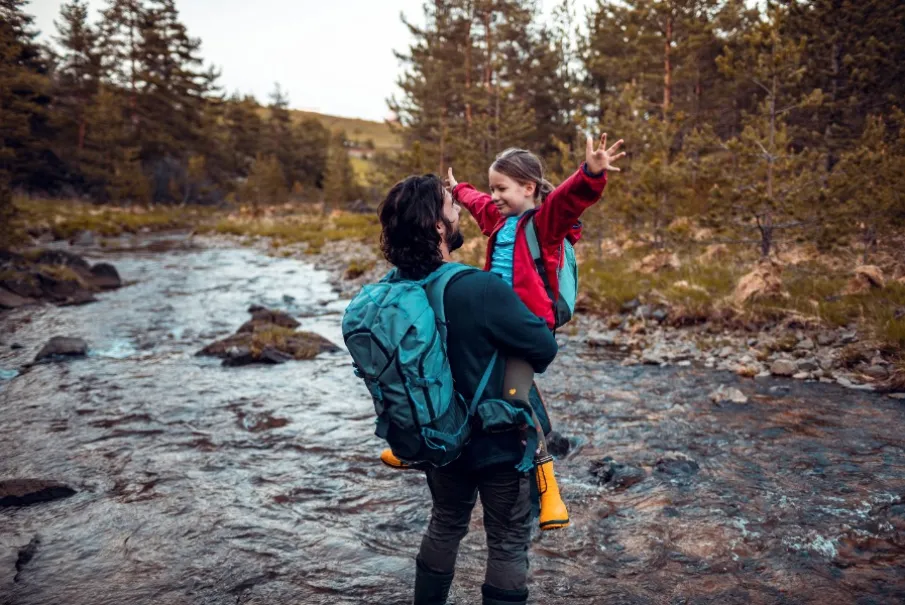 Father and daughter enjoying a hike near a stream in a forest with backpacks