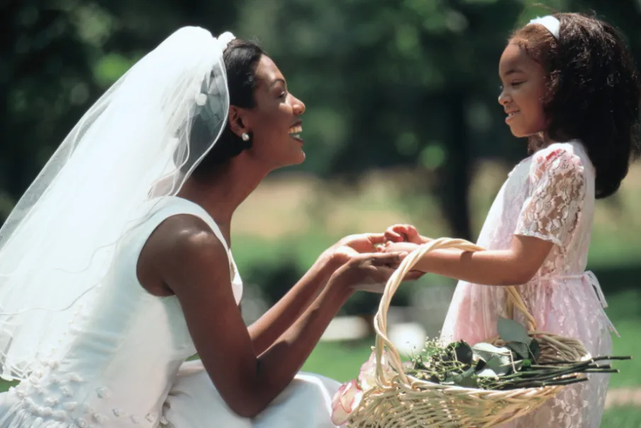 Bride smiling at young flower girl holding a basket of flowers outdoors
