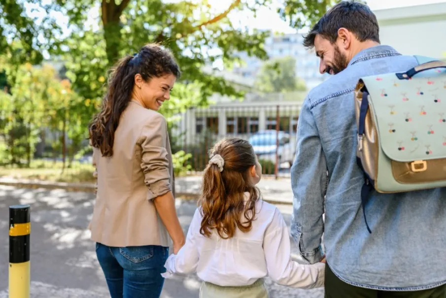 Family walking together outdoors with school bag and holding hands in a park.