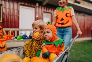Children in pumpkin and tiger costumes holding pumpkins in a wheelbarrow during Halloween.