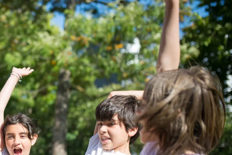 Children playing and smiling outdoors with raised hands
