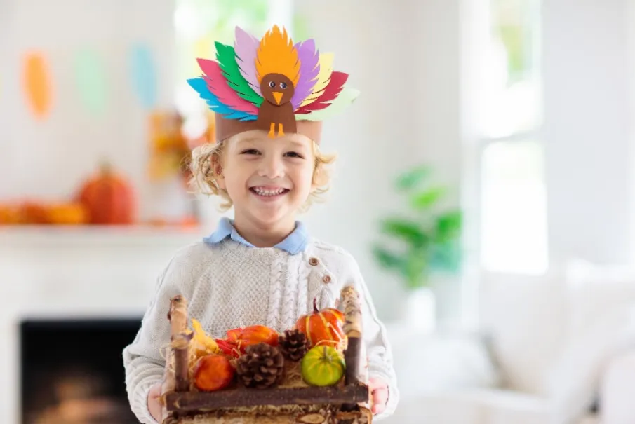 Child wearing a turkey headband holding a basket of autumn decorations