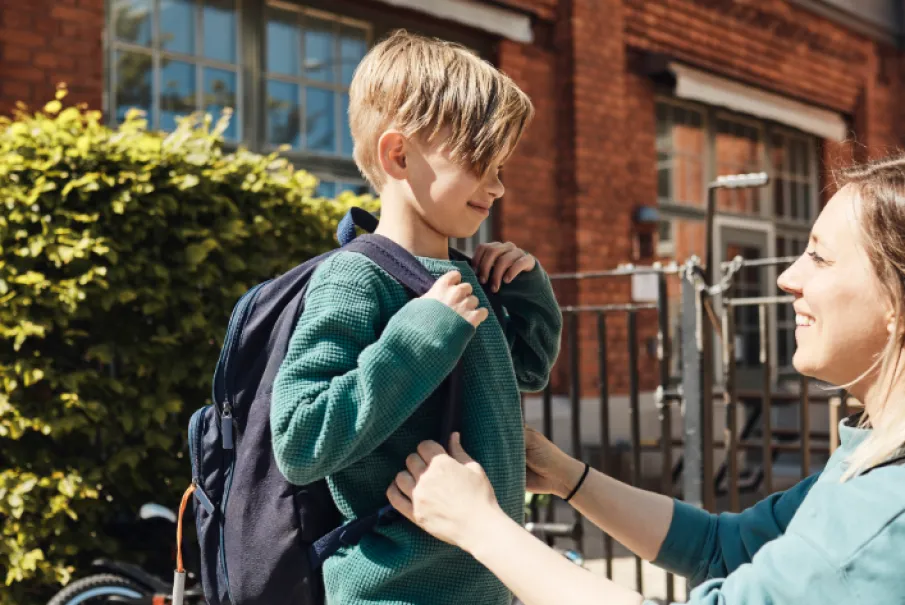 Woman helping her child with a backpack outdoors