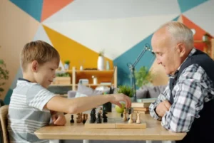 Boy playing chess with grandfather in a colorful room.
