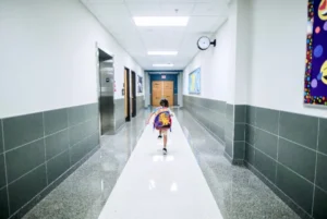 Young child with colorful backpack running down school hallway.