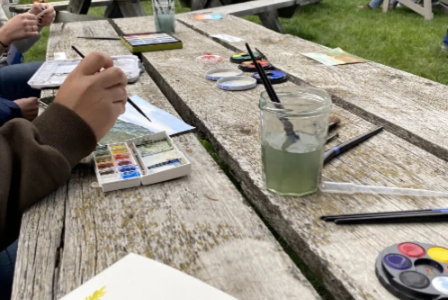 Outdoor painting activity at picnic tables with art supplies and watercolor illustrations