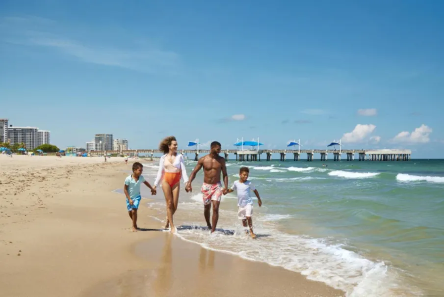 Family walking on a sunny beach near a pier and ocean waves