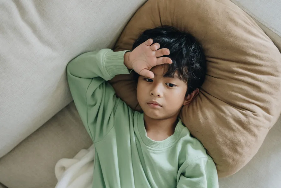 Unwell child resting on a couch with hand on forehead.