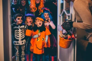 Excited children in Halloween costumes trick-or-treating at a door.