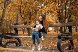 Mother and daughter reading a book on a park bench in fall.