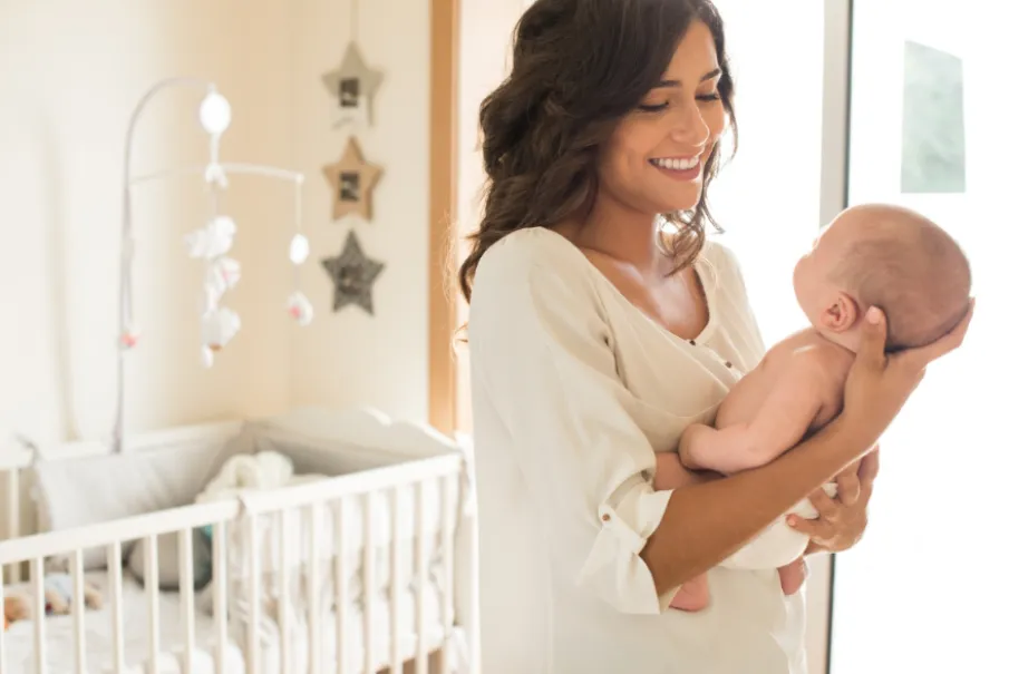 Smiling mother holding baby in cozy nursery