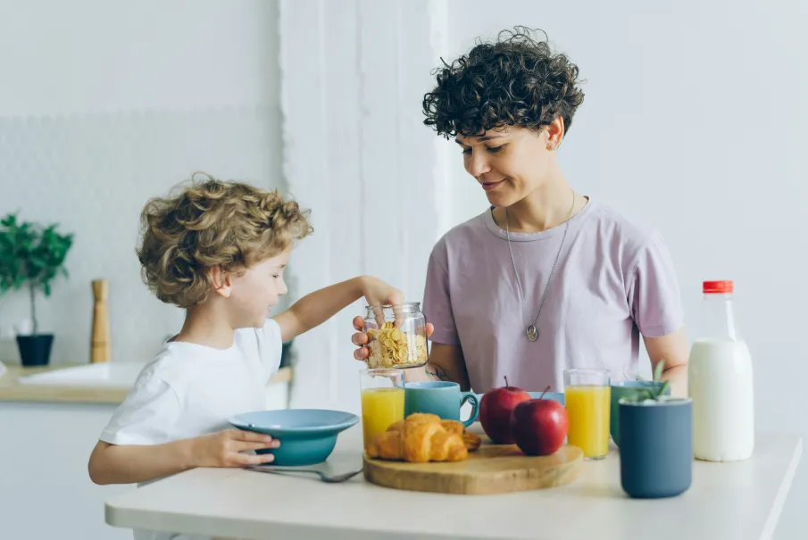 Child and adult preparing breakfast together at a kitchen table with croissants
